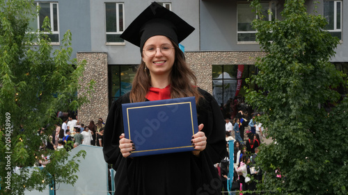 happy young woman graduate with diploma posing on the background of university, graduation, higher education, blue diploma, modern university building