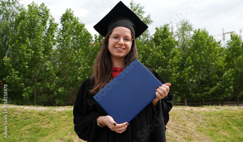 happy young female graduate with diploma posing outside
