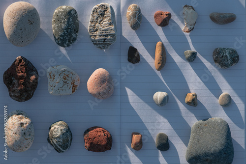 Various colorful pebbles and sea stones collected from the beach organized on a notebook and a zen stone balance tower on the rocky shore of Batumi Georgia during a sunny day