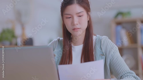 Young asian woman studying or working on a laptop in a modern home office space. Pensive concentrated girl sits at home.  pondering a solution, doubting question decision-making process.