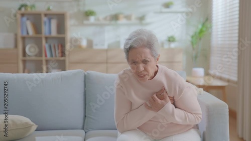 elderly woman experiences chest pain and acute heart failure on the couch due to a heart attack from cardiac arrest, older or patient with difficulty breathing due to vascular. medical emergency