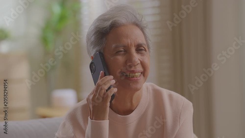 Smiling older woman talking mobile phone call conversation at home on sofa retired lady grandmother senior female talk smartphone receiving family sit on sofa at home.