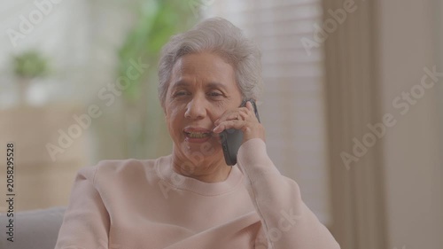 Smiling older woman talking mobile phone call conversation at home on sofa retired lady grandmother senior female talk smartphone receiving family sit on sofa at home.