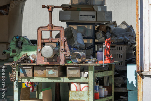 Canvas Print Cluttered workshop workbench with vintage hinged pipe vise and cutter surrounded by spare parts, assorted hardware, boxes, and various other materials used in heavy-duty metalwork