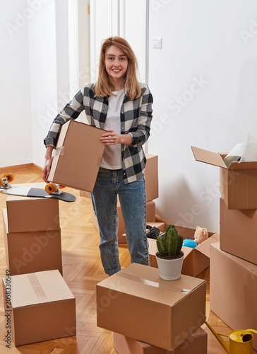 Smiling woman carrying moving box in new apartment