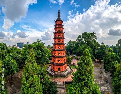 Aerial view of a vibrant orange pagoda surrounded by lush green trees under a cloudy blue sky