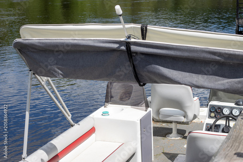 Close up view of the helm and seating area of a pontoon boat docked on a calm river.