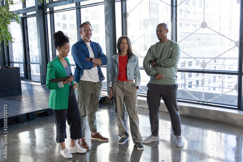 Diverse coworkers in casual clothes standing near metal windows in office holding tablet and phone