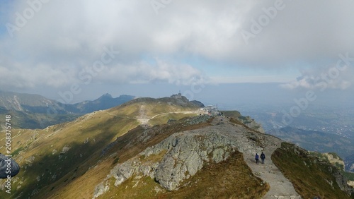 Scenic landscape of a high mountain hiking trail in the Tatra National Park, with a distant view of the Kasprowy Wierch station and observatory under a cloudy sky, Zakopane, Poland.