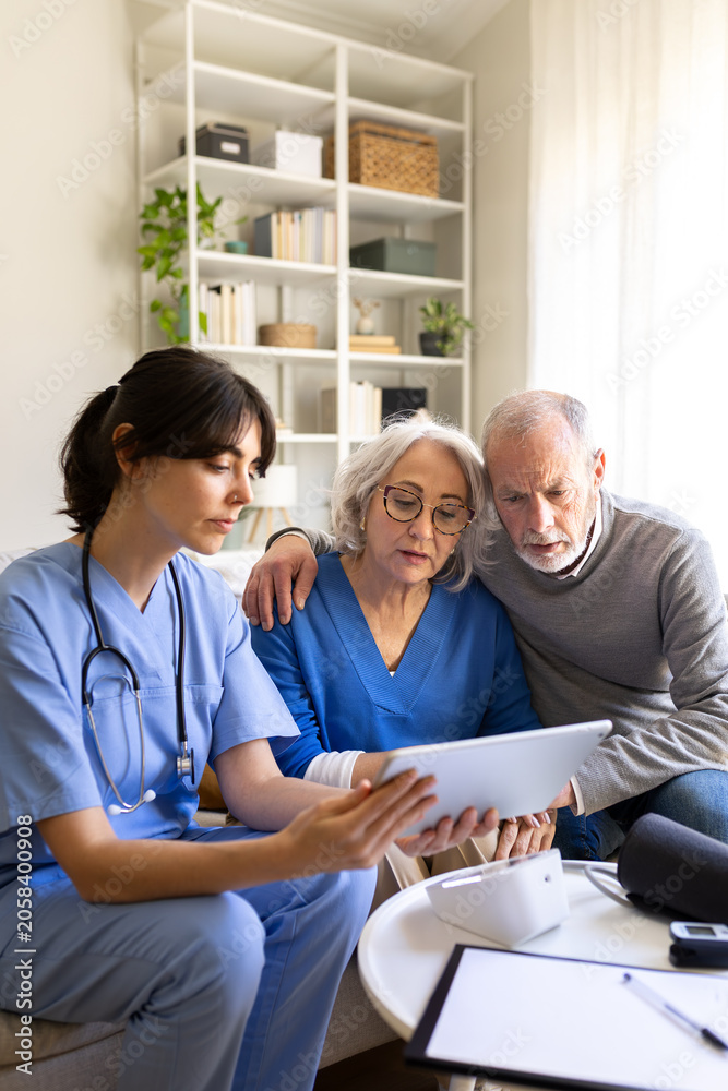 Obraz premium Nurse showing information on tablet to senior couple at home visit. Vertical image.