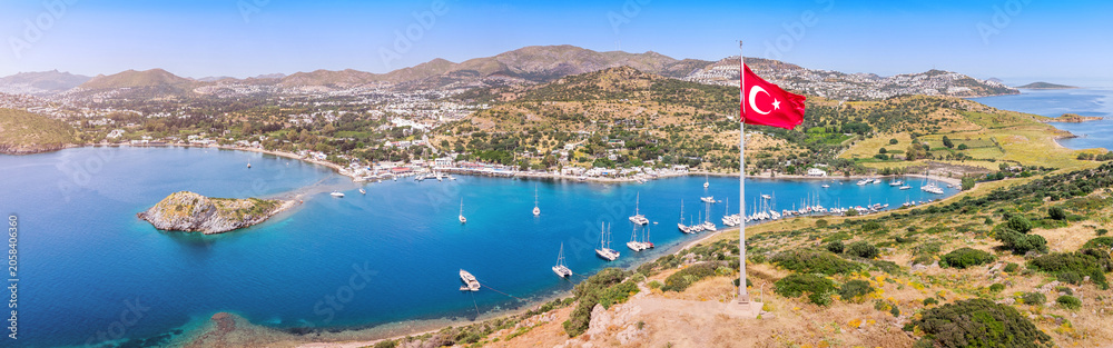 Obraz premium Bodrum Gumusluk bay panorama with a Turkish flag and many sailboats in the Aegean Sea on a sunny day