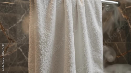 White towel hanging on a metal rack in a bathroom with stone walls and steam in the air