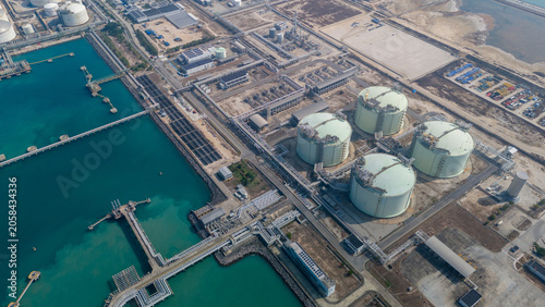 petrochemical plant and oil storage terminal  featuring numerous large white cylindrical tanks and spherical gas reservoirs situated along a coastal industrial zone.