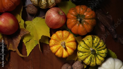 Warm autumn still life with pumpkins, apples, walnuts and pinecones on dark wooden table soft directional light creates rich orange tones, scattered yellow leaves, shallow depth of field, editorial