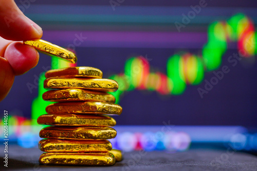 Close up investor hand stacking gold bullion bars with financial stock market graph background