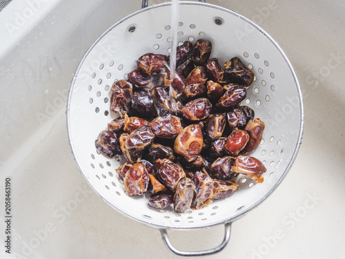 Dried brown dates in a colander under running water in the kitchen sink. Concept of healthy eating and using natural sweeteners. View from above. Ideal for nutrition, vegan diet, cooking content