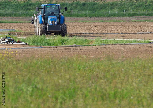 Slika na platnu Powerful blue tractor parked on grass in farm field