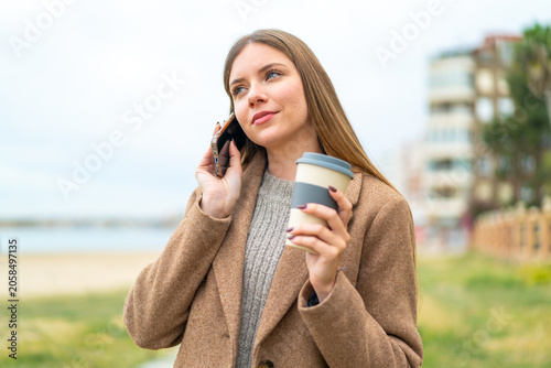 Canvastavla Young pretty blonde woman using mobile phone and holding a coffee