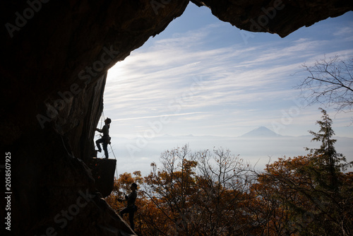 Silhouette of rock climbers on a cliff framed by cave opening with Mount Fuji and autumn foliage in Japan