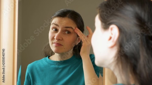 Woman looking in mirror and examining wrinkles on her forehead and around eyes.