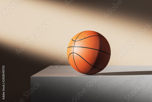 Basketball ball standing on minimal concrete pedestal under dramatic spotligh...
