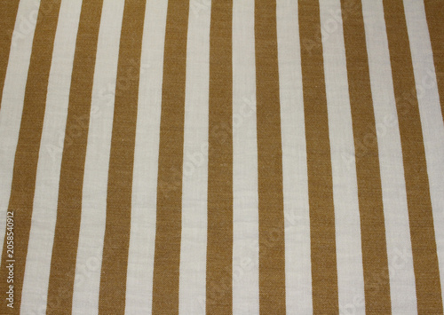 Close up of wrinkled light brown and white vertical striped fabric. Texture of crumpled classic caramel color striped polyester cloth background. 