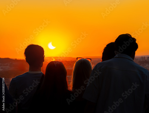 Schilderij op canvas Silhouettes of people backlit by the light, observing a partial solar eclipse at sunset from the top of the Eiffel Tower