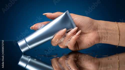 Close-up of a hand gently holding a silver tube with soap bubbles, reflecting on a dark surface