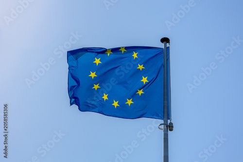 The flag of Europe on the pole waving in the air with blue sky as background, European union flag consists of twelve golden stars forming a circle on a blue field, A symbol for the whole of Europe.
