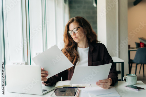 Fotografía Woman reviewing documents at a laptop in a bright home office while working remo