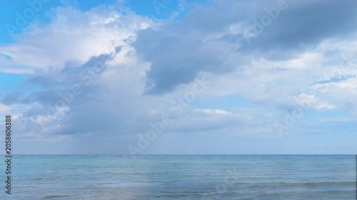 time-lapse of rain clouds on sunny blue sky over slow motion rippled sea water surface, empty idyllic seascape background for travel and beach holidays