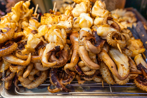 Grilled squid tentacles on metal rack at asian street food market for local culinary business and traditional seafood cuisine concept