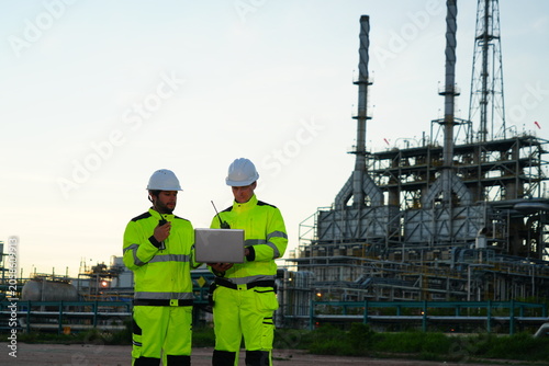 Male Caucasian engineers and their male foreman colleagues, all in uniform and helmets, are discussing and planning inspections of maintenance work while standing at an oil storage tank 