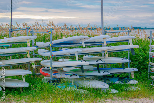 Bild auf Leinwand Racks with SUP boards and surfboards stored outdoors on the riverbank or lake coast on a summer day