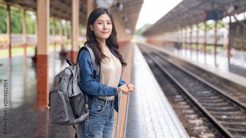 Photos Young Asian woman traveler waiting at railway station platform with backpack