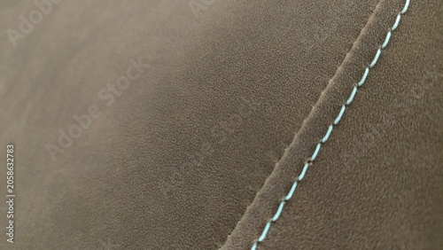 Close up of brown suede fabric texture featuring neat light colored decorative stitching. Concept of luxury interior design, upholstery, craftsmanship, textile quality, and automotive upholstery detai