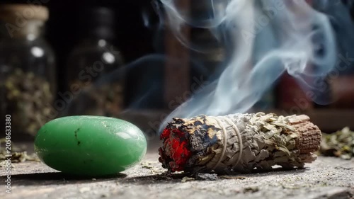 Burning Sage Smudge Stick With Green Jade Stone On Rustic Wooden Table In Dark Atmosphere