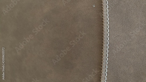 Close up of brown suede fabric texture featuring neat light colored decorative stitching. Concept of luxury interior design, upholstery, craftsmanship, textile quality, and automotive upholstery detai