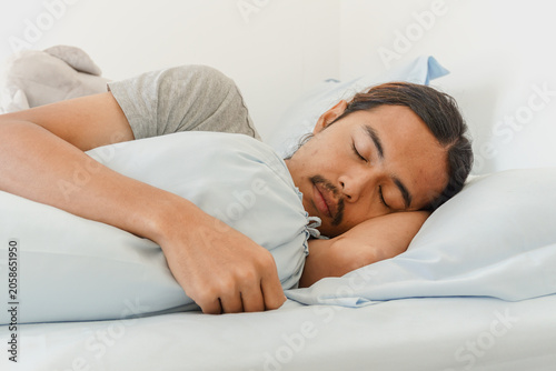 Obraz na plátne Young asian man with long hair and mustache sleeping peacefully in bed with a bo