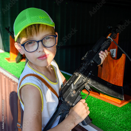 Φωτογραφία portrait of a boy in glasses and a bright green cap with a black automatic rifle