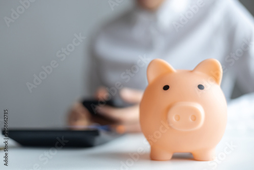Person working on a financial plan with a piggy bank in focus on a table in a bright indoor space during the day