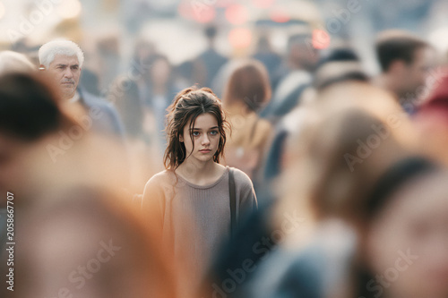 Young woman with pensive gaze, standing in a soft focus urban crowd