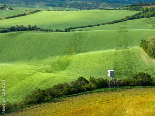 Aerial view of rolling green hills in Moravia with a wooden hunting tower