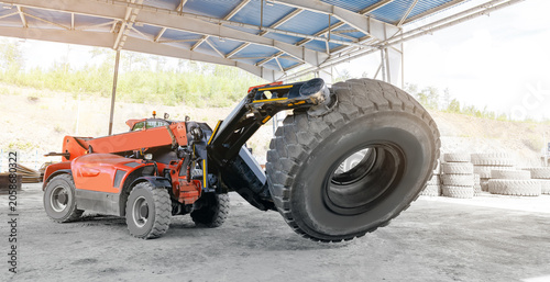 Telehandler lifting oversized tire inside covered industrial yard, changing wheels on quarry truck