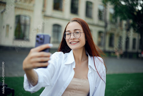 Businesswoman holds phone while smiling during video call outside a building in sunlight