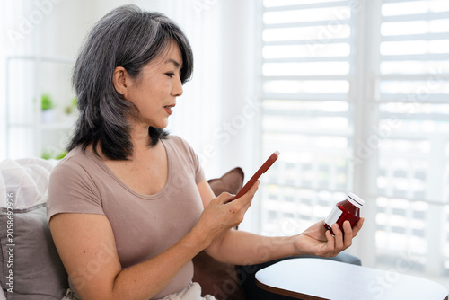 Asian woman holding bottle of food supplement or medicine using computer typing searching online prescription  pill bottle  information online.