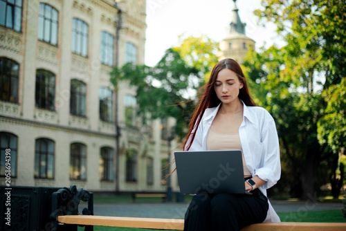 Young woman works on laptop outside at university campus in sunny weather during the day