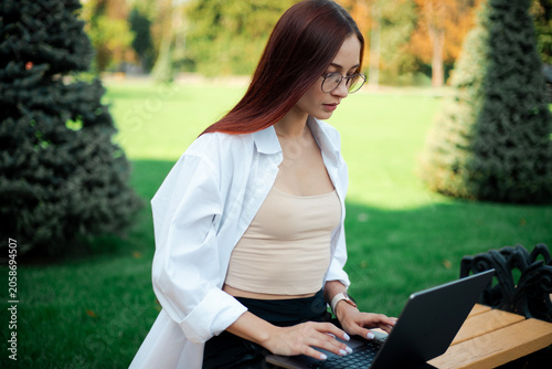 Woman works on laptop while sitting on bench in green park on sunny day