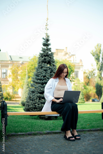 Woman works on laptop while sitting on bench in green park on sunny day