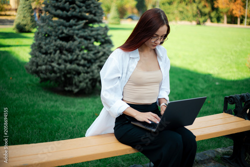 Woman works on laptop while sitting on bench in green park on sunny day